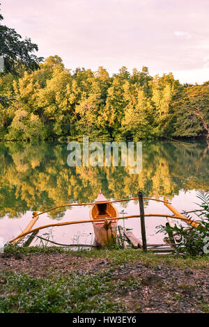 Un pêcheur traditionnel bateau amarré la pompe en place que les couchers de soleil sur une rivière bordée d'arbres comme miroir. Banque D'Images