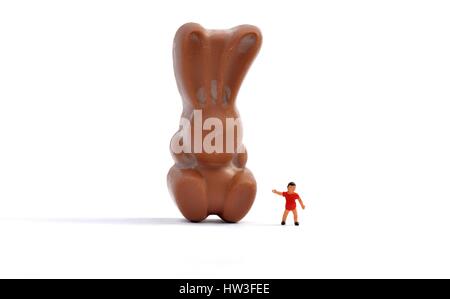 Une figurine miniature garçon debout à côté d'un lapin en chocolat. Banque D'Images