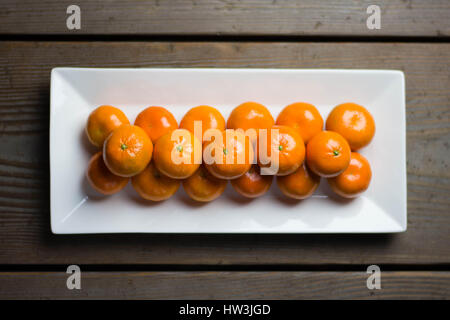 Les tangerines symétriquement alignées sur plaque blanche avec table rustique en arrière-plan. Banque D'Images