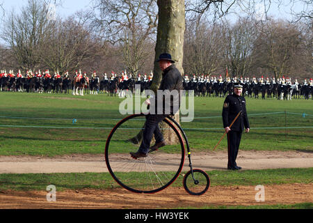 Londres, Royaume-Uni. Mar 16, 2017. Un homme sur un Penny Farthing les balades à vélo le long en tant que membres de HM Household Cavalry parade pour l'examen général majeur dans Hyde Park, Londres. La cavalerie de famille est composée des deux plus hauts régiments de l'armée britannique, les bleus et les Royals et des gardiens de la vie. Ils seront vus dans de nombreux engagements royale cette année. Ils ont été inspectés par le Major-général Ben Bathurst, l'officier général commandant l'armée à Londres et la reine des soldats, ce matin, à Hyde Park, Londres le 16 mars 2017. Crédit : Paul Marriott/Alamy Live News Banque D'Images