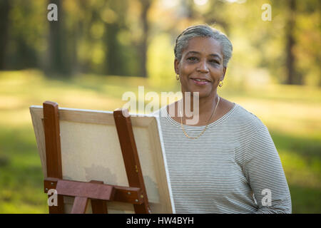 Portrait of Black woman painting on canvas in park Banque D'Images