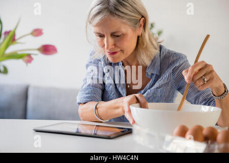 Caucasian woman baking with recette sur digital tablet Banque D'Images