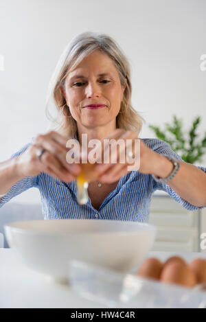 Caucasian woman cracking oeuf dans bol Banque D'Images