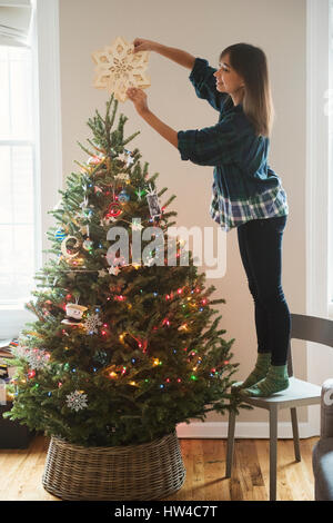 Mixed Race woman plaçant star ornament on top of Christmas Tree Banque D'Images