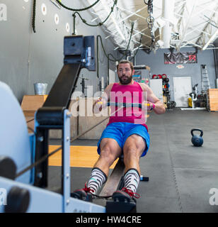 Mixed Race man using rowing machine in gymnasium Banque D'Images