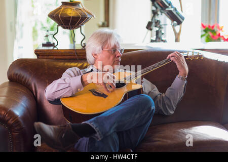 Young man playing guitar on sofa Banque D'Images