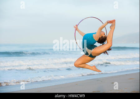 Young gymnast jumping with hoop on beach Banque D'Images