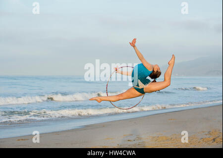 Young gymnast jumping with hoop on beach Banque D'Images