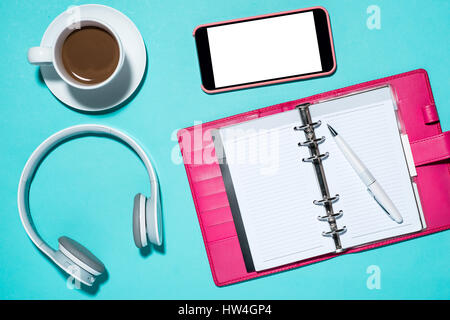 Les fournitures de bureau. Vue de dessus sur l'ordinateur portable ouvert, stylo, casque, smartphone, et une tasse de café sur le bleu. Banque D'Images