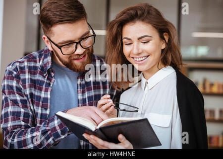 Smiling young man and woman se préparer pour les examens ensemble dans library Banque D'Images