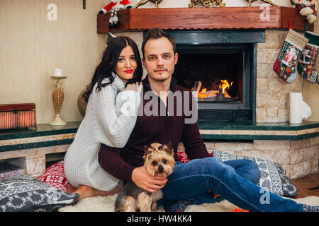 Beau couple avec petit chien amoureux près de cheminée Banque D'Images