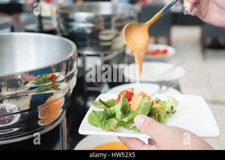 Cuillère à soupe crémeuse de Thousand Island Dressing étant versé sur de la salade du jardin frais dans le petit-déjeuner buffet à l'hôtel. Banque D'Images