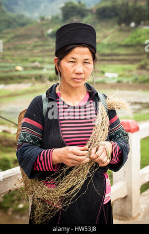 Sapa, SAPA, Vietnam - 5 mai 2014 : le portrait de femme Hmong tribaux dans les vêtements nationaux debout sur la route près de rizières avec foin dans le ha Banque D'Images