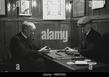 1940s, historique, deux hommes âgés dans un coin d'un bar public lambrissé de bois, l'un portant une casquette en tissu, l'autre fumant un pipe, jouant un jeu de dominos, Angleterre, Royaume-Uni. Banque D'Images