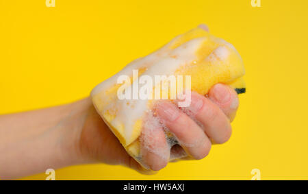 La main avec une éponge avec de la mousse sur fond jaune Banque D'Images