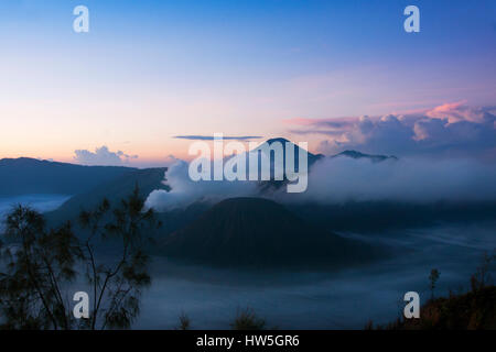 La fumée blanche qui sort des volcans entouré par des nuages blancs de brume et un ciel bleu clair vu à une distance dans le matin du Mont Penanjakan à Banque D'Images