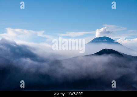 La fumée blanche qui sort des volcans entouré par des nuages blancs de brume et un ciel bleu clair vu à une distance dans la matinée. Banque D'Images