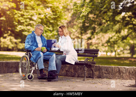 Caring nurse talking with patient in wheelchair contrôler l'historique de la maladie Banque D'Images