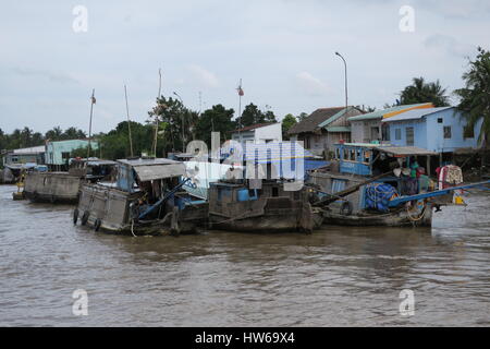 Mékong en Indochine, il vous suffit de bateau en bois sur la rivière sale avec des maisons sur des piliers colorés voile unique. Banque D'Images