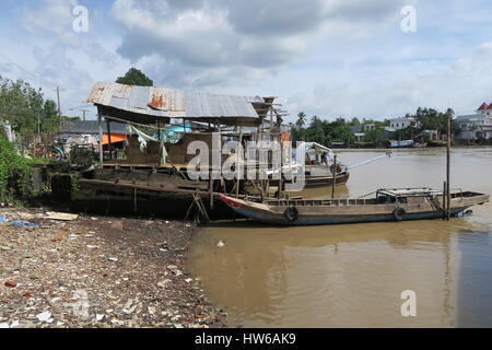 Mékong en Indochine, il vous suffit de bateau en bois sur la rivière sale avec des maisons sur des piliers colorés voile unique. Banque D'Images