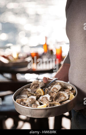 L'homme tient un plateau d'huîtres crues dans un restaurant en bord de mer Banque D'Images