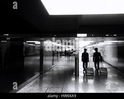 Coup franc de deux pilotes dans un corridor de l'aéroport. Style rétro noir et blanc image montrant une vue arrière de l'pilotes avec leurs bagages, rubrique towa Banque D'Images