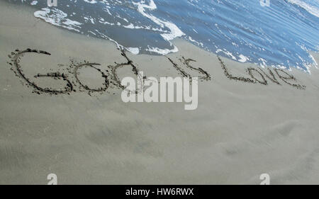 Dieu est Amour écrit dans le sable que les vagues se laver près de lui. Banque D'Images