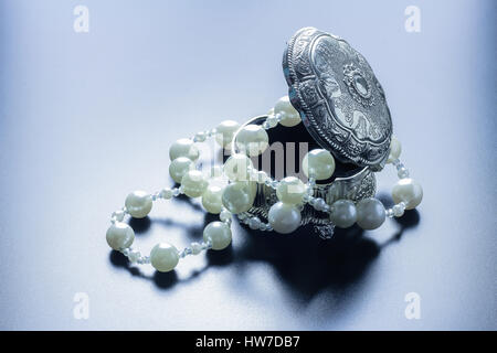 Photo d'une boîte de bijoux en argent avec perles blanches tourné avec projecteurs et fond noir Banque D'Images