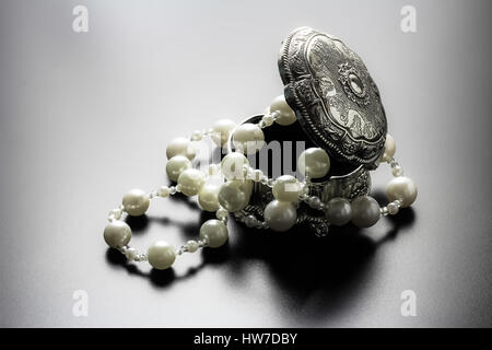 Photo d'une boîte de bijoux en argent avec perles blanches tourné avec projecteurs et fond noir Banque D'Images