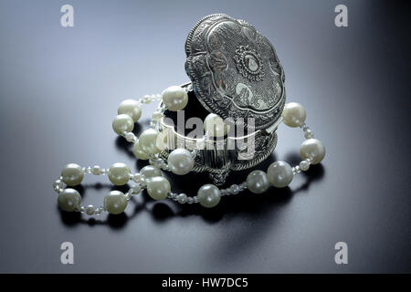 Photo d'une boîte de bijoux en argent avec perles blanches tourné avec projecteurs et fond noir Banque D'Images