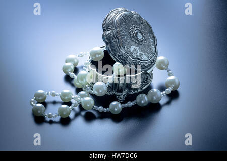 Photo d'une boîte de bijoux en argent avec perles blanches tourné avec projecteurs et fond noir Banque D'Images