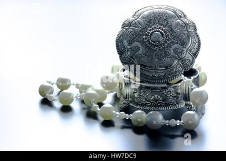 Photo d'une boîte de bijoux en argent avec perles blanches tourné avec projecteurs et fond noir Banque D'Images