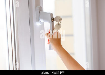 La main de l'enfant sur la sécurité d'un handle de fenêtre avec clé Banque D'Images