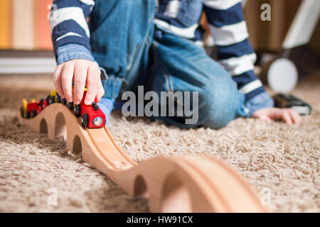 Détail d'un petit Garçon jouant avec train en bois à l'intérieur, sur un tapis. Réduire la profondeur de champ. Banque D'Images