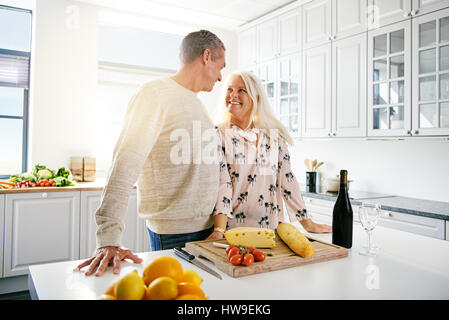 Les cadres supérieurs l'homme et la femme au comptoir de la cuisine se tenant ensemble avec du fromage, des fruits et du vin en face d'eux Banque D'Images
