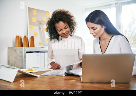 Deux jeunes femmes d'affaires attrayant partenaires travaillant à la paperasse pagination par un magazine ou d'un rapport qu'ils analyser et planifier leurs études de marché Banque D'Images