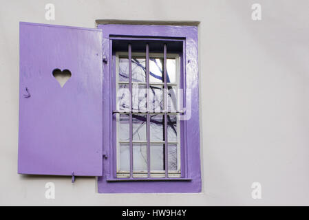 Violet clair pastel cadre en bois avec fenêtre en forme de coeur sur l'obturateur et le fer grinçant sur un mur blanc Banque D'Images