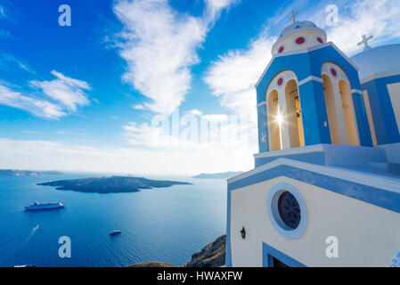 Soleil qui brille à travers d'une église à clocher en vue de Santorini Caldera volcanique et des bateaux en elle, Santorini, Cyclades, Grèce Banque D'Images