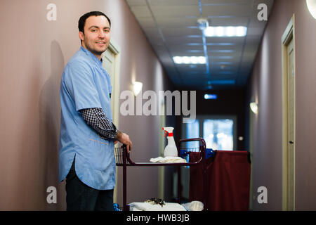 Un homme qui est sur l'équipe de nettoyage le personnel est souriant avec une serviette vide dans le processus de nettoyage de l'hôtel Chambres et la prestation de haut-knotch service pour les invités. Banque D'Images