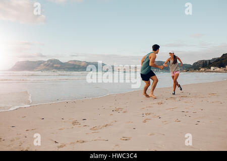 Shot de fit jeune couple jouant sur la plage. Jeune homme et femme en marche et jouer au bord de la mer. Banque D'Images