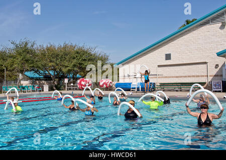 Groupe de femmes (tous âges) fréquentant l'aérobic aquatique, de l'instructeur de classe, à l'aide de la démonstration de "l'eau en styromousse noodles', piscine extérieure chauffée. Banque D'Images