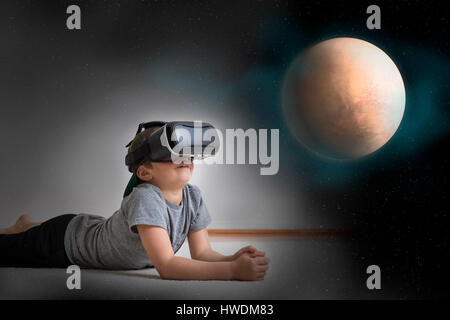 Jeune garçon couché sur le plancher, le port de casque de réalité virtuelle, à la recherche de planète, digital composite Banque D'Images