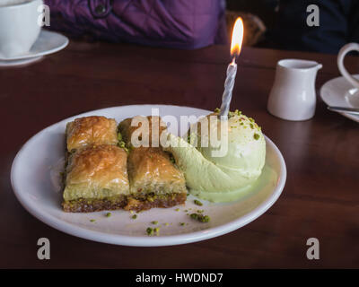 Quatre morceaux de Baklava sur une plaque dans un restaurant turc servi avec une boule de crème glacée à la pistache avec une seule bougie dans la glace comme une birthd Banque D'Images