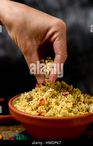 Libre d'un jeune homme obtenir certains taboulé, une salade arabe levantin typique, avec sa main d'un bol en terre cuite placé sur un set de table pour le déjeuner Banque D'Images