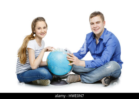 Beau garçon et fille de l'adolescence dans les tenues de assis sur le plancher à la recherche de quelque chose sur le globe de la Terre. Isolé sur fond blanc. Copier l'espace. Banque D'Images