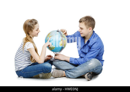 Beau garçon et fille de l'adolescence dans les tenues de assis sur le plancher à la recherche de quelque chose sur le globe de la Terre. Isolé sur fond blanc. Copier l'espace. Banque D'Images