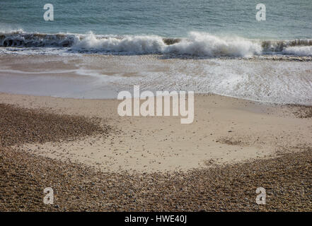 Une vague se brisant sur une plage de sable avec des cailloux sur la rive Banque D'Images