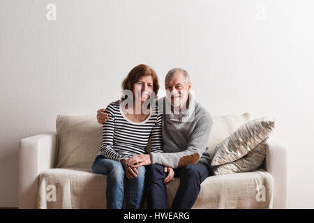 Belle senior couple sitting on couch, serrant. Studio shot. Banque D'Images