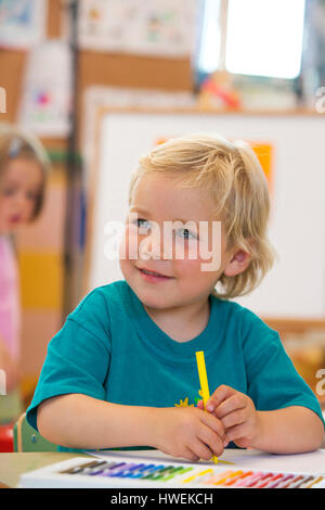 Garçon d'âge préscolaire avec stylo coloriage in classroom Banque D'Images