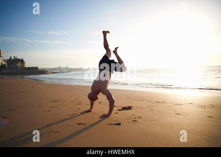 Man doing handstand sur la plage ensoleillée, Cascais, Portugal Banque D'Images